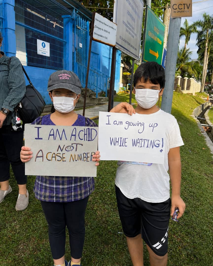 Two children holding signs that read I am a child, not a case number and I am growing up while waiting